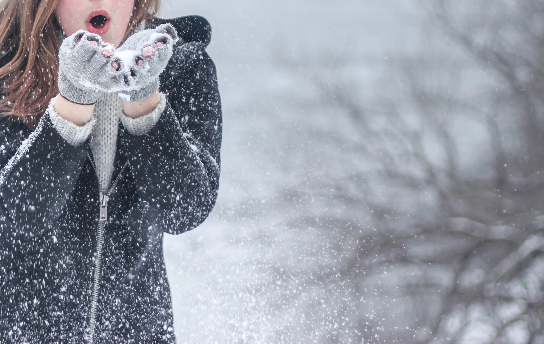 A person blowing snow from their gloved hands