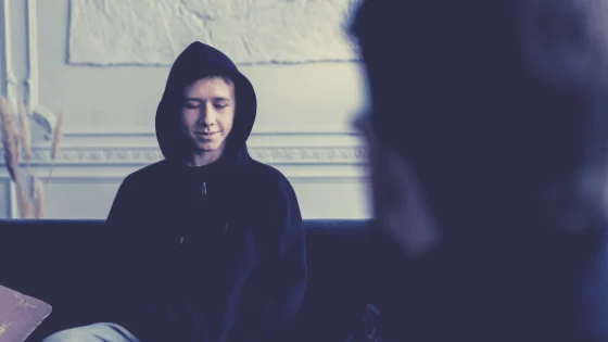 A person in a dark hooded top sitting across from someone